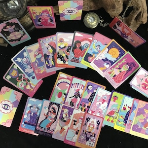 Op de afbeelding: Een verzameling kleurrijke tarotkaarten met diverse illustraties en titels zoals "De Keizerin" en "Koning van Pentakels". De kaarten hebben levendige kunstwerken in roze, blauwe en paarse tinten, met een vintage zakhorloge op de achtergrond.