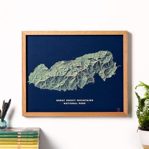 May include: A framed map of the Great Smoky Mountains National Park, with a blue background and green topographic lines. The map is framed in a natural wood frame.