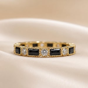Peut inclure: Une bague en or avec un motif alterné de pierres noires rectangulaires et de pierres claires rondes. Les bords métalliques de la bague présentent une texture perlée, et les pierres sont serties en rangée continue sur tout le pourtour de l'anneau.