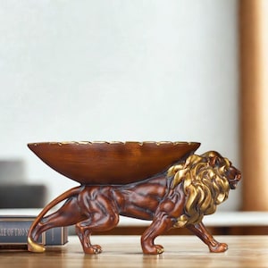 May include: A decorative lion sculpture with a brown body and gold accents. The lion is carrying a wooden bowl on its back. The sculpture is a unique home decor item.