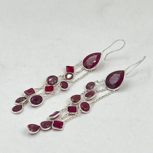 Peut inclure: Boucles d'oreilles pendantes ornées de pierres précieuses rouge rubis de différentes formes. Les boucles d'oreilles sont composées de chaînes en métal argenté et de fermoirs à crochet. Les pierres comprennent des formes de goutte, ovales et carrées.