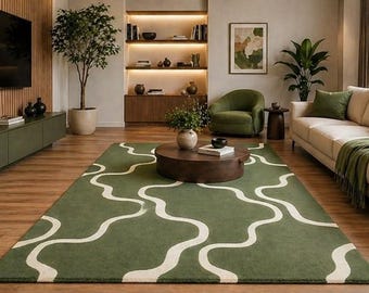 Pode incluir: Uma sala de estar com um tapete verde com um padrão ondulado branco. O quarto inclui um sofá bege com almofadas verdes e uma manta verde, uma poltrona verde e uma mesa de centro de madeira. Uma TV grande está montada na parede.