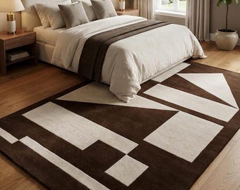 May include: A rectangular area rug featuring a bold geometric pattern in dark brown and cream. The design consists of large, angular shapes, including triangles and rectangles, arranged across the surface to create a high-contrast visual effect.