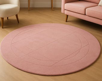 May include: A round, blush-colored rug with a geometric design. The rug features a series of curved and straight lines that create an abstract pattern. The rug is placed on a hardwood floor, and is surrounded by furniture.