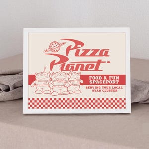 May include: A framed print featuring the red Pizza Planet logo with a planet icon, three three-eyed alien characters, and the text Food & Fun Spaceport Serving Your Local Star Cluster, finished with a red and white chequered border at the bottom.