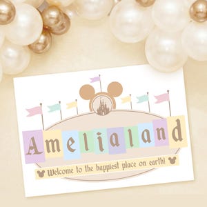 May include: A sign that reads "Amelialand" in pastel colors, with a Mickey Mouse head and castle design. The sign also says "Welcome to the happiest place on earth!" and is surrounded by balloons.