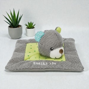 May include: A gray teddy bear plush toy with a light green and white polka dot square, and a gray border. The bear has blue and green accents on its ears. The text "MY LITTLE" is printed on the blanket.