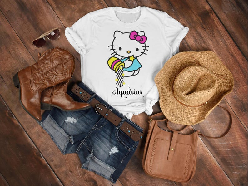 以下が含まれることがあります： 白いTシャツに漫画の猫のデザインと「Aquarius」の文字。画像には、デニムショーツ、茶色のカウボーイブーツ、麦わら帽子、茶色の革のバッグ、サングラスが含まれています。