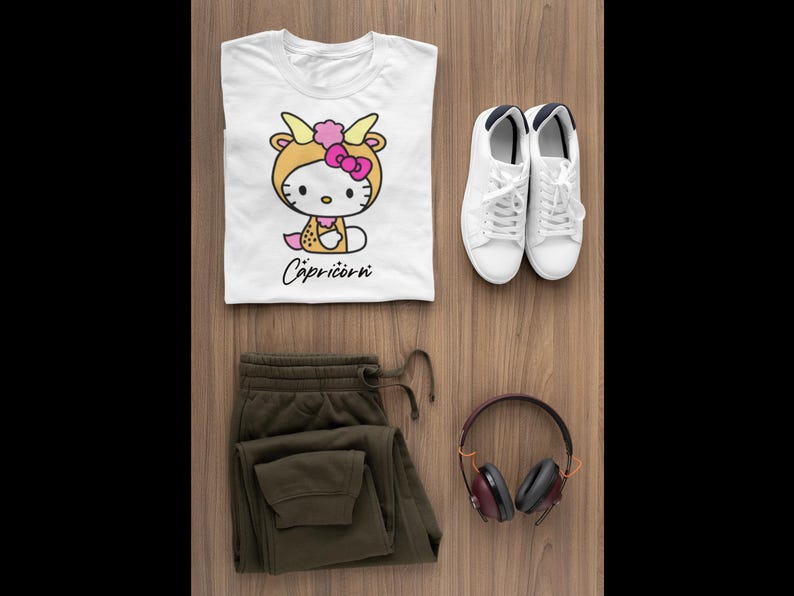 May include: A flat lay featuring a white t-shirt with a Capricorn graphic, olive green joggers, white trainers, and maroon headphones. The t-shirt displays a cartoon character in a Capricorn costume. The word "Capricorn" is written in cursive.
