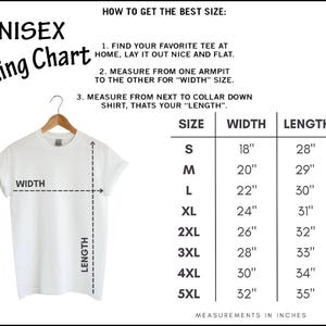 以下が含まれることがあります： 木製のハンガーに掛けられた白いTシャツ。"UNISEX Sizing Chart"のグラフィックが表示されています。サイズS（幅18インチ、長さ28インチ）から5XL（幅32インチ、長さ35インチ）までの幅と長さのインチ単位の測定値が記載されています。