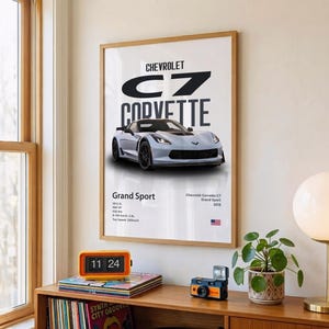 May include: A framed print featuring a light blue Chevrolet C7 Corvette Grand Sport. The print includes the car's name, specifications, and the Chevrolet logo. The print is displayed on a wall above a wooden shelf.