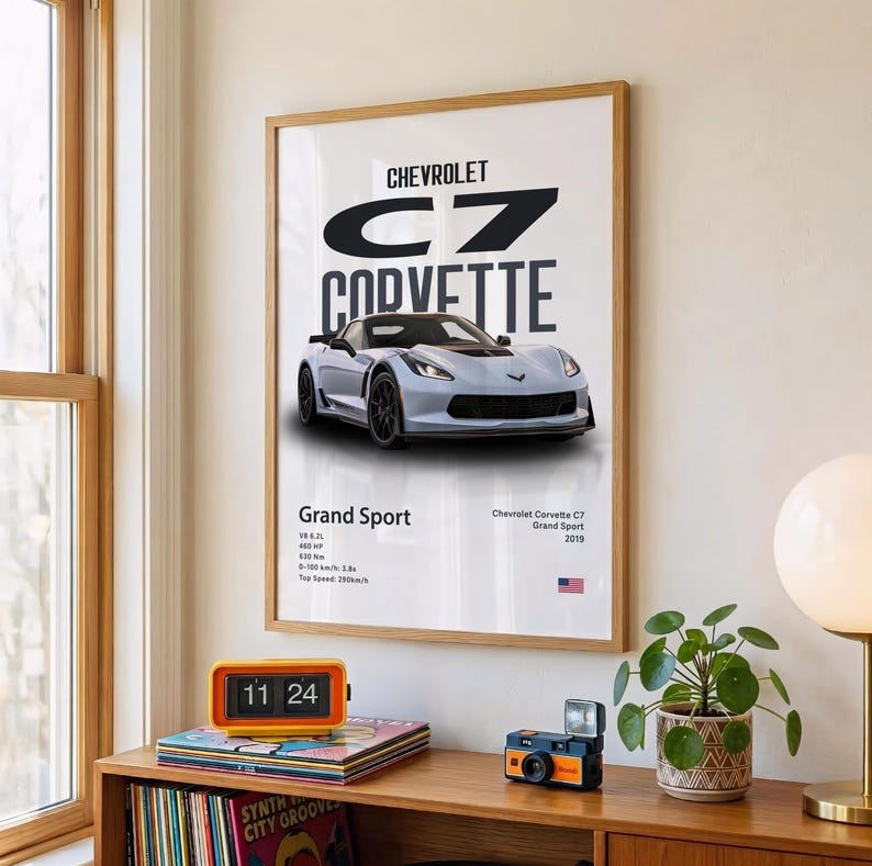 May include: A framed print featuring a light blue Chevrolet C7 Corvette Grand Sport. The print includes the car's name, specifications, and the Chevrolet logo. The print is displayed on a wall above a wooden shelf.