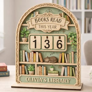 May include: A wooden bookshelf-shaped counter with the text "BOOKS READ THIS YEAR" and "OLIVIA'S LIBRARY". The counter displays the number 136. The design includes miniature books, plants, and a sleeping cat. The color scheme is primarily beige and green.