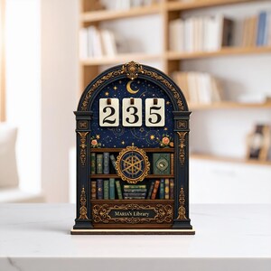 Op de afbeelding: Een decoratief houten boekenrek met de nummers 235. Het marineblauwe rek heeft een hemels ontwerp, een gouden kompas en miniatuurboeken. De tekst "MARIA'S Library" staat onderaan.