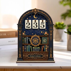 Op de afbeelding: Een decoratieve houten eeuwige kalender met een hemels ontwerp. De kalender toont de nummers 235 op witte kaarten. Het ontwerp omvat een boekenplank, een maan, sterren en de tekst "MARIA'S Library".
