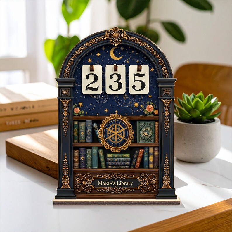 Op de afbeelding: Decoratieve houten kalender met een hemels ontwerp. Het heeft een marineblauwe achtergrond, gouden accenten en de nummers 235. De kalender heeft een boekenplankontwerp met de tekst "MARIA'S Library".
