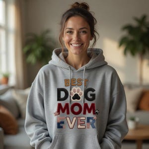 Peut inclure: Un sweat à capuche gris avec le texte "BEST DOG MOM EVER" dans un design coloré et superposé. Le mot "DOG" comporte une empreinte de patte à la place du "O". Le sweat à capuche a une capuche à cordon.