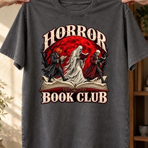 Peut inclure: Un t-shirt gris anthracite avec une illustration représentant une créature à tête de citrouille, un fantôme et un squelette lisant sur un livre ouvert. Le motif inclut une lune rouge, des arbres sombres et le texte HORROR BOOK CLUB en blanc.