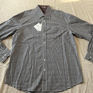 May include: A long-sleeved button-down shirt with a black and white checkered pattern. The shirt has a classic collar and cuffs with button closures. A tag is attached near the top button. The shirt is made of a lightweight fabric.