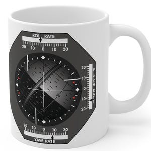 May include: A white ceramic mug with a black handle and the text "But First, Coffee" in a black, handwritten-style font. The mug is on a white surface.