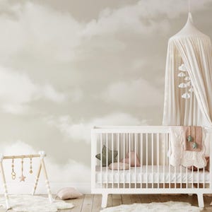 May include: A nursery scene featuring a white crib with a canopy and mobile. The crib is decorated with pillows and a blanket. A wooden play gym and a cloud-patterned wall complete the soft, neutral-toned room.
