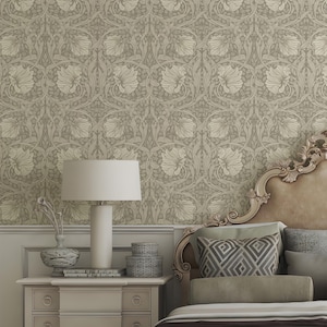 May include: A bedroom scene featuring a beige floral wallpaper as a backdrop. A nightstand with a white lamp, decorative vase, and stacked boxes sits beside a bed with decorative pillows and a carved headboard. The overall aesthetic is elegant and classic.