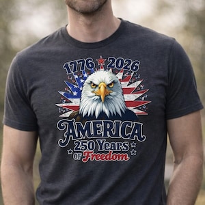 May include: Dark gray t-shirt featuring a detailed graphic of an American bald eagle with the text "1776 2026 AMERICA 250 Years of Freedom". The eagle has a stern expression, with a yellow beak and piercing eyes, set against a backdrop of the American flag.