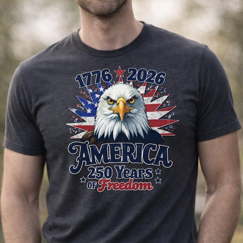 May include: Dark gray t-shirt featuring a detailed graphic of an American bald eagle with the text "1776 2026 AMERICA 250 Years of Freedom". The eagle has a stern expression, with a yellow beak and piercing eyes, set against a backdrop of the American flag.