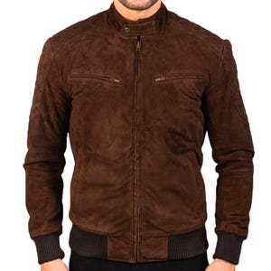 May include: A brown suede bomber jacket with a stand-up collar and a front zipper closure. The jacket features two front pockets with zippers and ribbed cuffs and hem. The jacket is a rich, dark brown color.