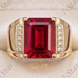 Op de afbeelding: Een gouden ring met een grote, rechthoekige, smaragdgeslepen rode edelsteen in het midden, geflankeerd door twee verticale rijen kleine, heldere, rondgeslepen accentstenen. De ring wordt gepresenteerd in een donkerhouten doosje.