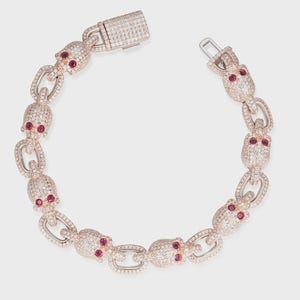 May include: A rose gold bracelet featuring skull-shaped links encrusted with clear crystals. Each skull has red gemstone eyes. The bracelet is connected by oval links and has a crystal-covered clasp.