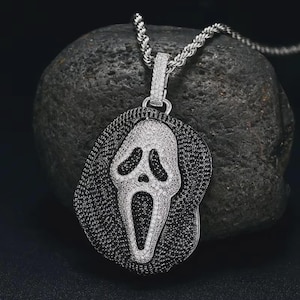 Puede incluir: Collar con colgante plateado con diseño de máscara de Scream. El colgante está incrustado con piedras preciosas blancas y negras, con una cadena plateada a juego. El colgante mide aproximadamente 5 cm de largo.