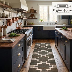 Puede incluir: Una cocina con gabinetes azul oscuro, encimeras de madera y una alfombra con diseño. Ollas de cobre cuelgan sobre la estufa. La alfombra tiene un diseño geométrico en tonos grises y blancos. La cocina es de estilo rústico.