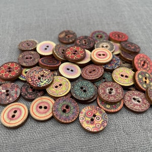 May include: A collection of assorted wooden buttons with decorative patterns in various colors. The buttons have two or four holes for sewing and feature floral, geometric, and abstract designs. The buttons are round and oval-shaped.
