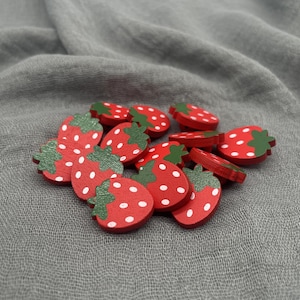 May include: A collection of small, wooden strawberry-shaped embellishments. Each strawberry is painted red with white dots and a green stem. These decorative pieces are ideal for crafting and scrapbooking projects.
