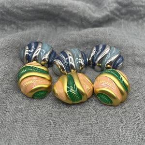 May include: Six vintage clip-on earrings. Three are blue and silver, with a ribbed design. The other three are gold, with pink and green stripes. The earrings have a rounded, domed shape.