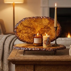 Puede incluir: Una bandeja de madera con borde natural sostiene dos velas encendidas y un candelabro alto con una vela encendida. La bandeja está sobre una mesa de madera. Una pieza decorativa de madera y libros están sobre la mesa.