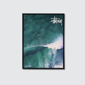May include: Framed art print showing a surfer on a large wave in the ocean. The image is predominantly teal and white, with a surfer in a black wetsuit. The Stussy logo is in the upper right corner.