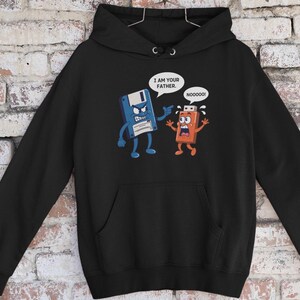 Może przedstawiać: Czarna bluza z kapturem z komiksowym wzorem. Niebieska dyskietka mówi "I AM YOUR FATHER" do pomarańczowego pendrive'a, który odpowiada "NOOOOOO!". Projekt jest parodią słynnej sceny filmowej.