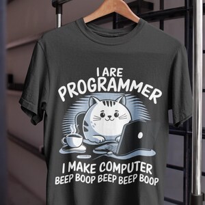 Può includere: T-shirt nero con la grafica di un gatto che usa un laptop, una tazza di caffè e il testo "I ARE PROGRAMMER I MAKE COMPUTER BEEP BOOP BEEP BOOP". Il gatto è bianco con strisce grigie.