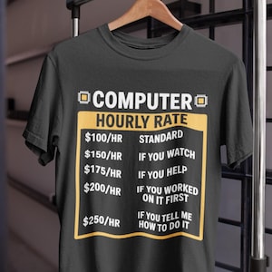 Peut inclure: T-shirt noir avec l'inscription "COMPUTER HOURLY RATE" en blanc et jaune. Le t-shirt indique les tarifs horaires des services informatiques, allant de 100 €/h à 250 €/h, selon le niveau d'implication. Le t-shirt est suspendu à un cintre en bois.