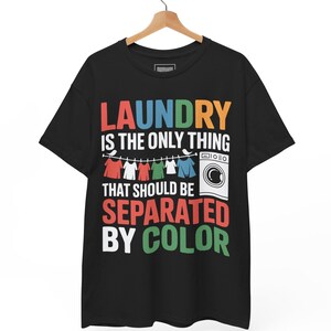 May include: Black t-shirt with the text "LAUNDRY IS THE ONLY THING THAT SHOULD BE SEPARATED BY COLOR" in colorful block letters. The design includes a clothesline with hanging shirts and a washing machine graphic.