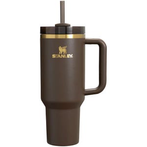 May include: A brown Stanley tumbler with a handle and straw. The tumbler has a gold rim and the Stanley logo in gold. The tumbler is designed to keep drinks cold or hot. The tumbler is made of stainless steel.