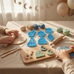 Peut inclure: Une table avec de la pâte à modeler, des rouleaux à pâtisserie et des emporte-pièces bleus de différentes formes. Des outils en bois, une planche à découper en bois avec des formes de pâte et des ballons sont également présents. Une activité créative.