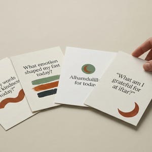 Może przedstawiać: Cztery białe karty z tekstem i minimalistycznymi ilustracjami. Karty zawierają frazy takie jak "Czy moje słowa odzwierciedlały dziś życzliwość?" i "Za co jestem wdzięczny na iftarze?" Ręka trzyma jedną kartę.