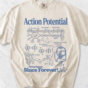 May include: An ivory short-sleeve t-shirt featuring a blue graphic print of a neuron diagram with the text Action Potential and Firing Signals Since Forever! The design includes scientific illustrations of dendrites, axons, and ion channels.