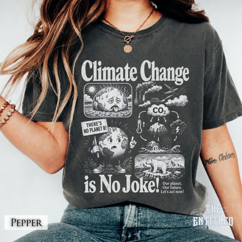 May include: A charcoal gray t-shirt featuring a graphic print with the text Climate Change is No Joke. The design includes illustrations of a sweating earth, a polar bear, CO2 emissions, and a sign that reads There's No Planet B.