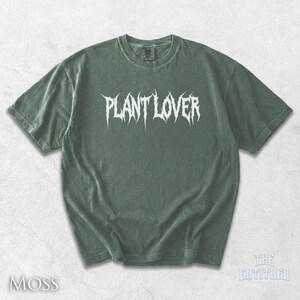 以下が含まれることがあります： モスグリーンのTシャツ。白いゴシック体で「PLANT LOVER」と書かれています。クルーネックと半袖です。左下に白で「MOSS」とプリントされています。