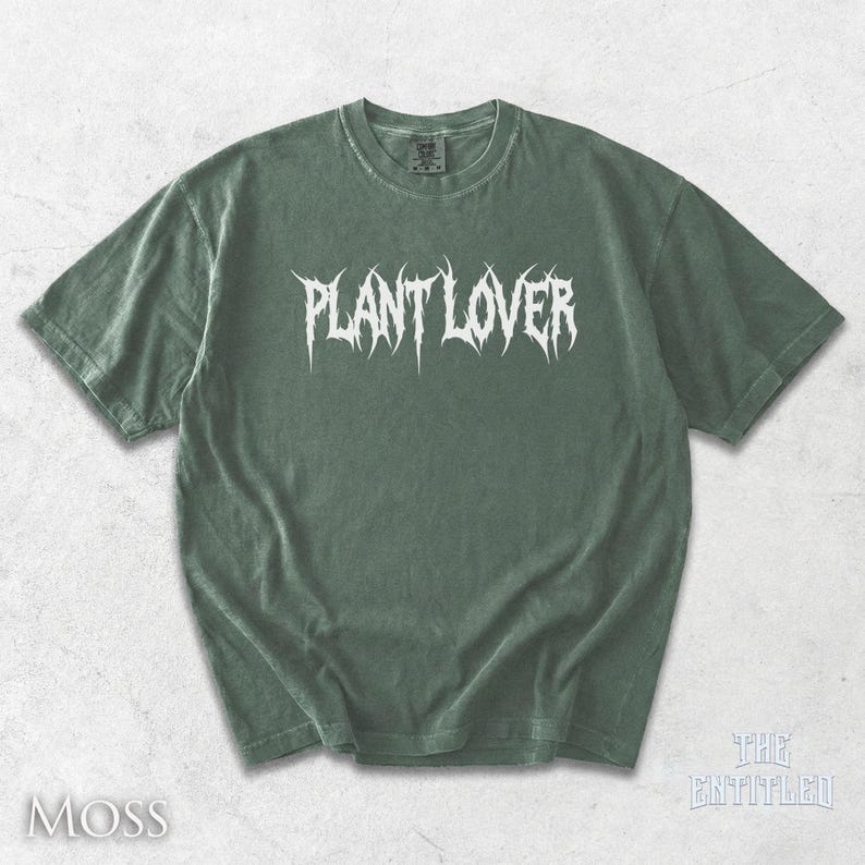 以下が含まれることがあります： モスグリーンのTシャツ。白いゴシック体で「PLANT LOVER」と書かれています。クルーネックと半袖です。左下に白で「MOSS」とプリントされています。