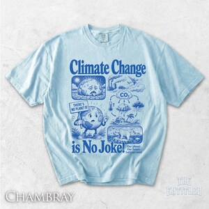 May include: A light blue t-shirt featuring a dark blue graphic print with the text Climate Change is No Joke! The design includes illustrations of a sad earth, a polar bear on ice, industrial smoke, and a sign reading There's No Planet B!
